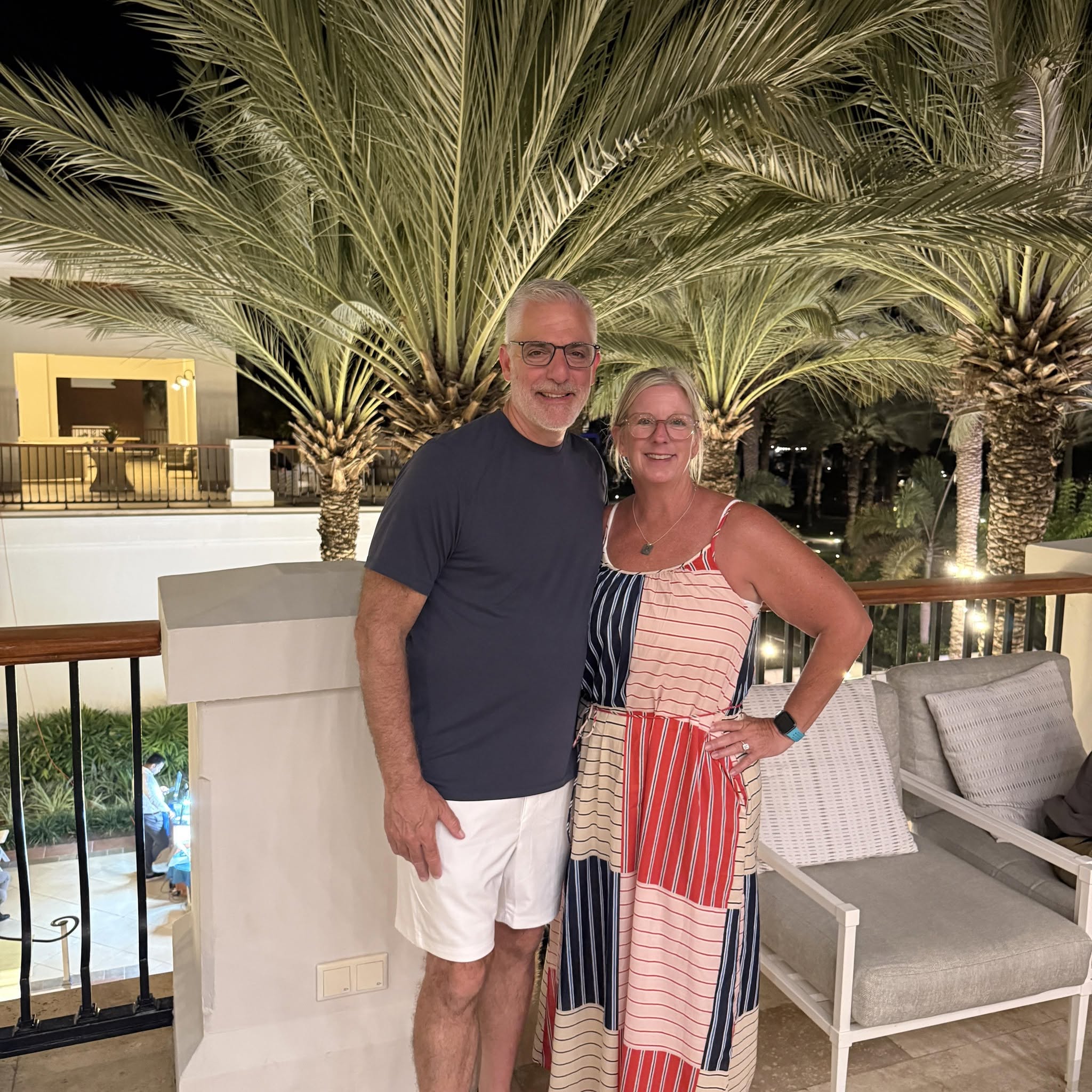 curacao rootop Smiling couple posing outdoors at night with large palm trees behind them on a patio/kitchen area.